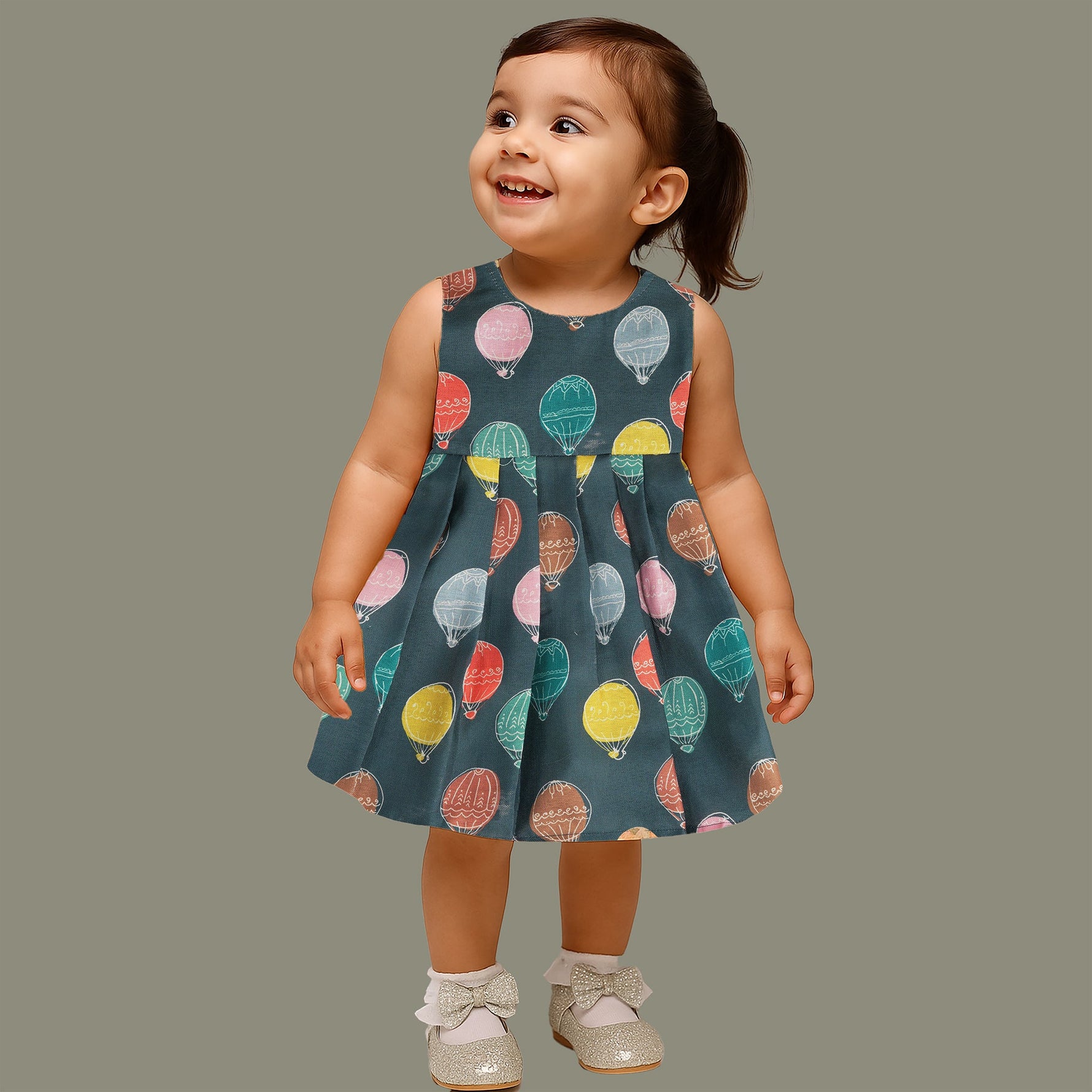 Little girl in a sleeveless denim blue frock with colorful balloon prints, made of slub cotton – part of Boon Babies babywear collection in Coimbatore.