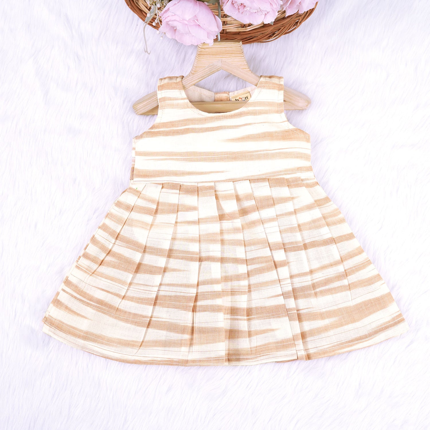 Smiling young girl wearing a sleeveless beige and white striped cotton frock from Boon Babies’ kidswear collection in Coimbatore – perfect for ages 6 months to 5 years.