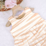 Smiling young girl wearing a sleeveless beige and white striped cotton frock from Boon Babies’ kidswear collection in Coimbatore – perfect for ages 6 months to 5 years.