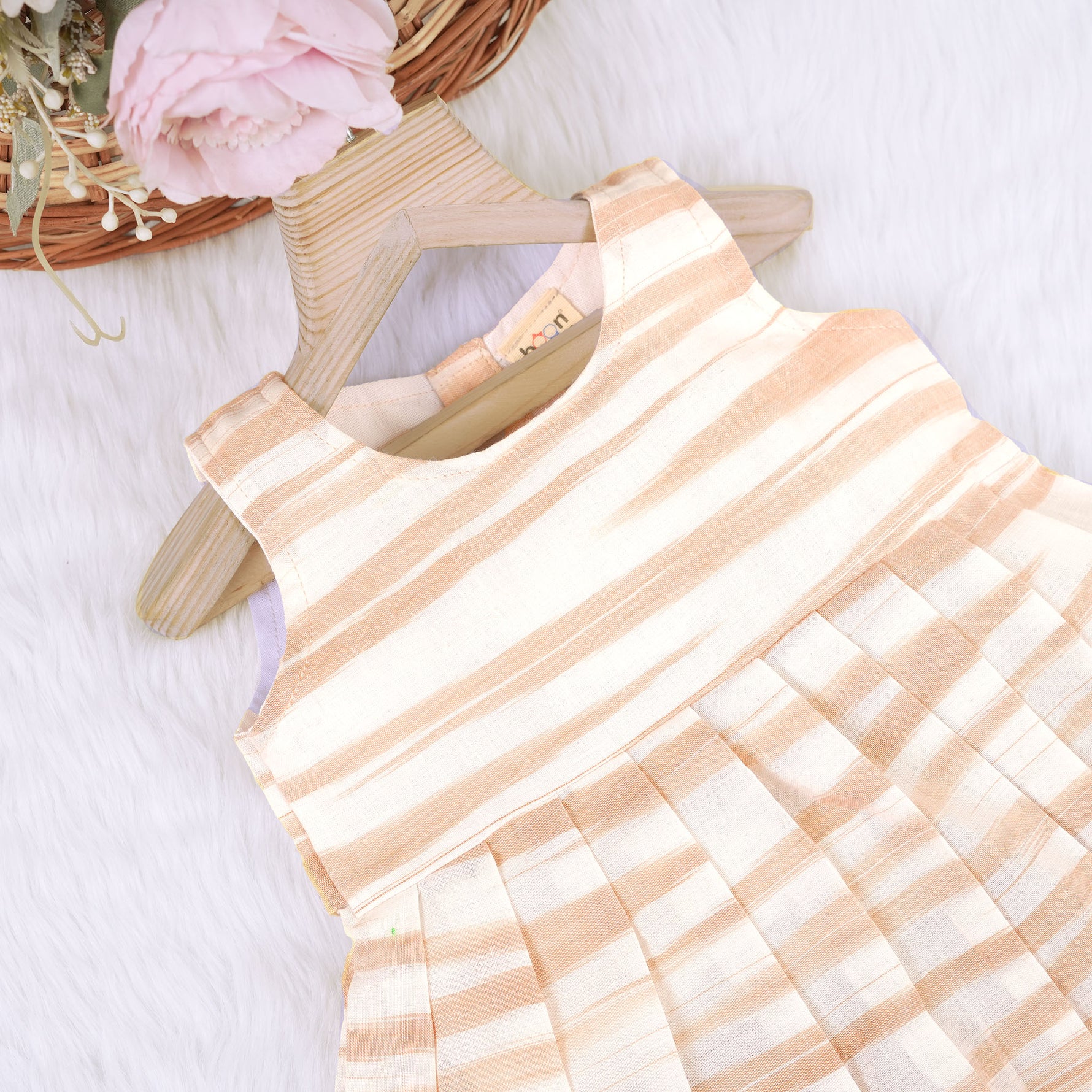 Smiling young girl wearing a sleeveless beige and white striped cotton frock from Boon Babies’ kidswear collection in Coimbatore – perfect for ages 6 months to 5 years.