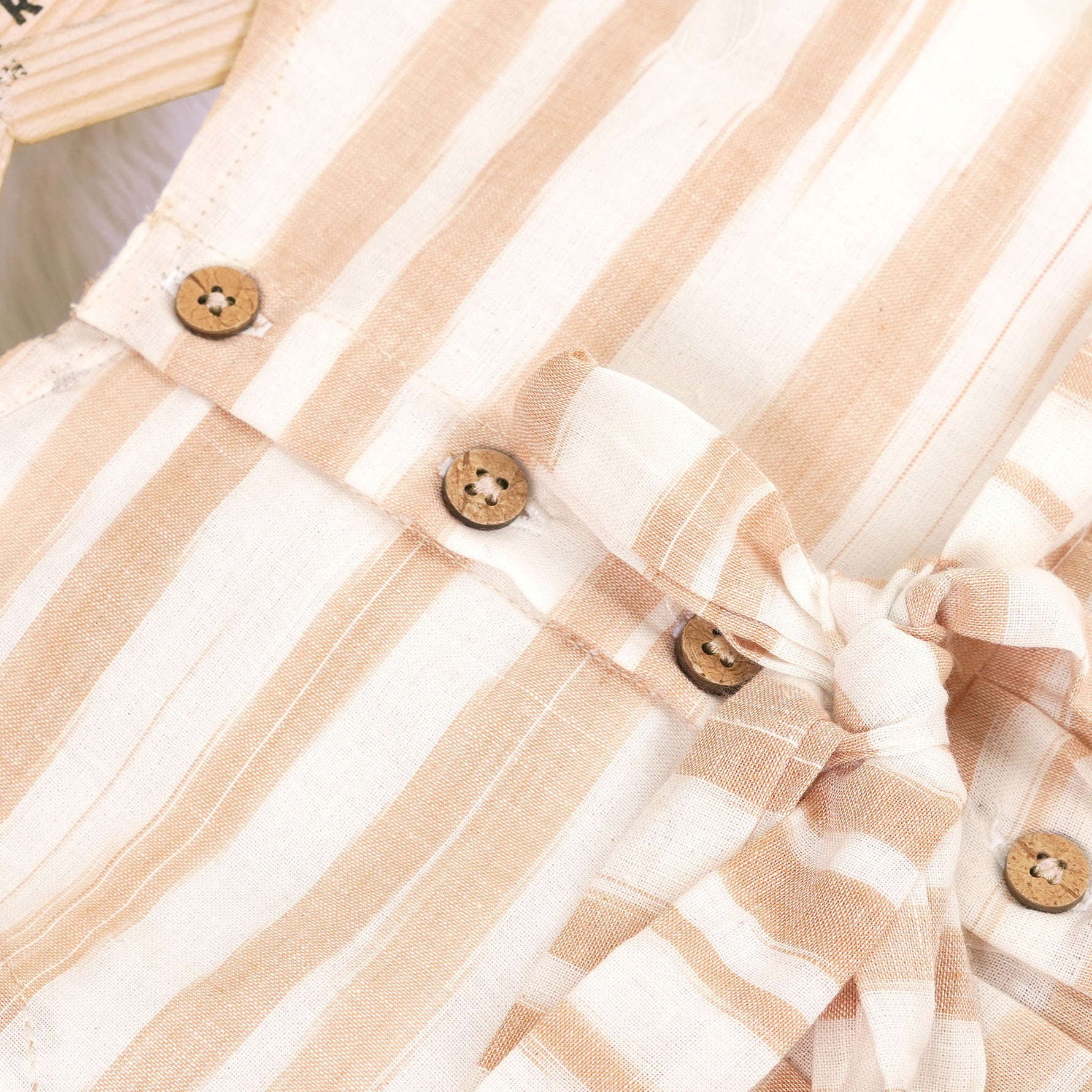 Smiling young girl wearing a sleeveless beige and white striped cotton frock from Boon Babies’ kidswear collection in Coimbatore – perfect for ages 6 months to 5 years.