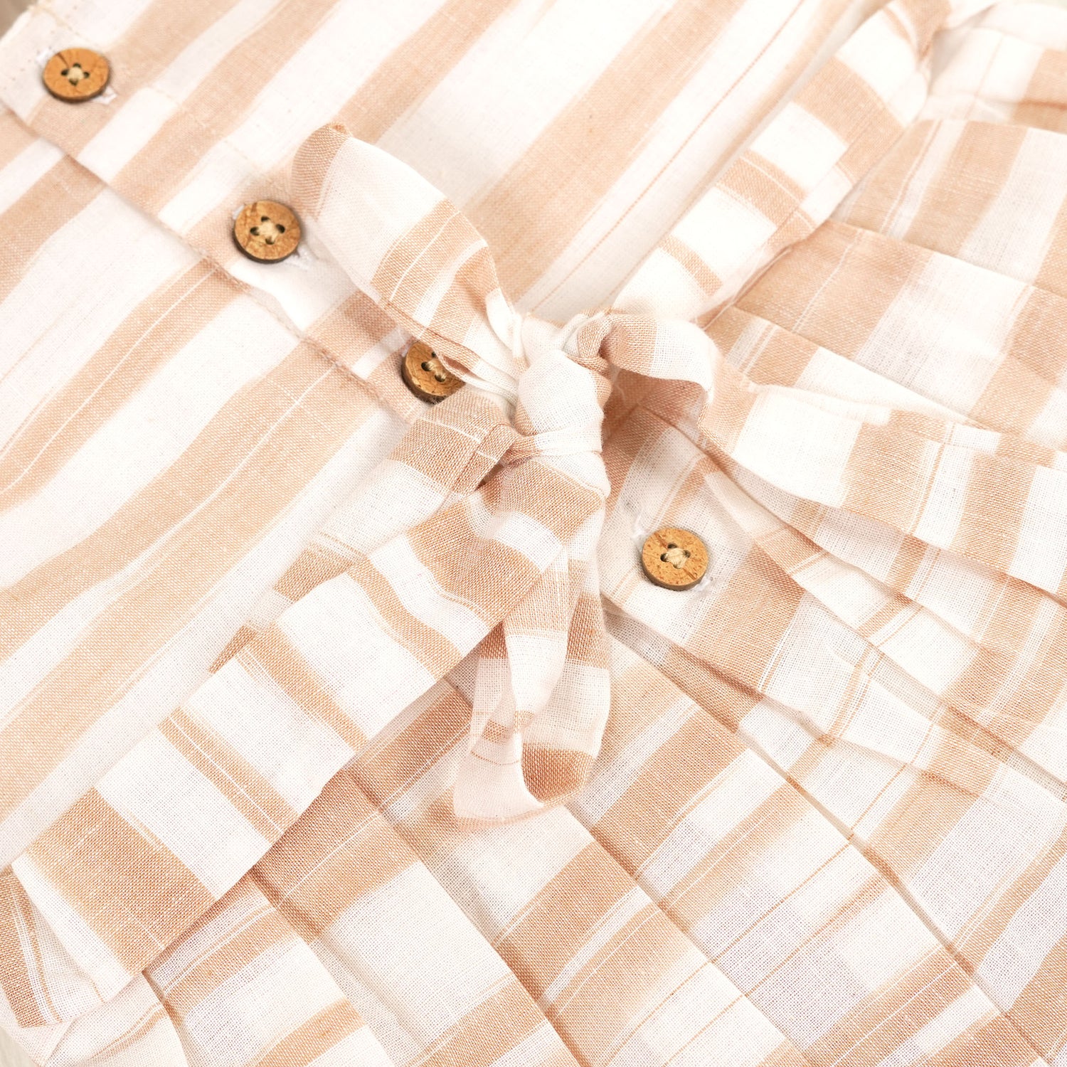 Smiling young girl wearing a sleeveless beige and white striped cotton frock from Boon Babies’ kidswear collection in Coimbatore – perfect for ages 6 months to 5 years.