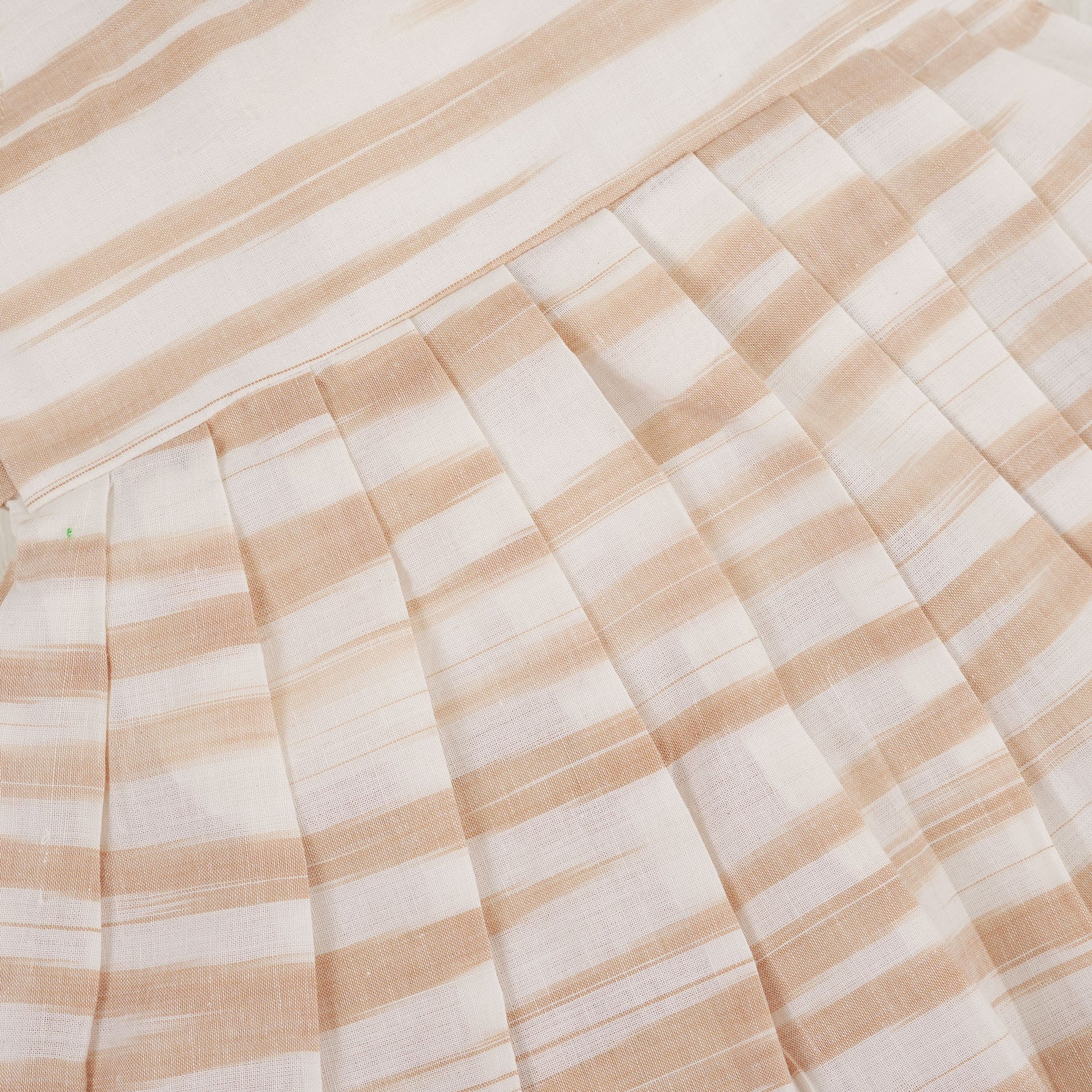 Smiling young girl wearing a sleeveless beige and white striped cotton frock from Boon Babies’ kidswear collection in Coimbatore – perfect for ages 6 months to 5 years.