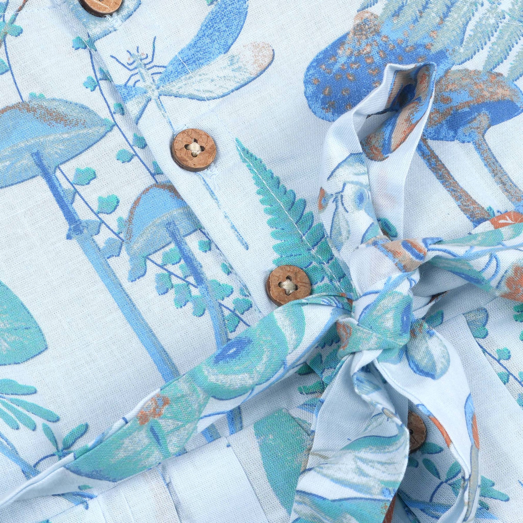 Girls' sleeveless frock in pastel blue cotton with butterfly and floral print, displayed with a wooden hanger under pink orchids – Boon Babies summer casual wear collection.
