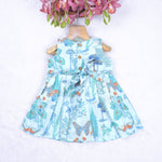 Girls' sleeveless frock in pastel blue cotton with butterfly and floral print, displayed with a wooden hanger under pink orchids – Boon Babies summer casual wear collection.
