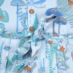 Girls' sleeveless frock in pastel blue cotton with butterfly and floral print, displayed with a wooden hanger under pink orchids – Boon Babies summer casual wear collection.
