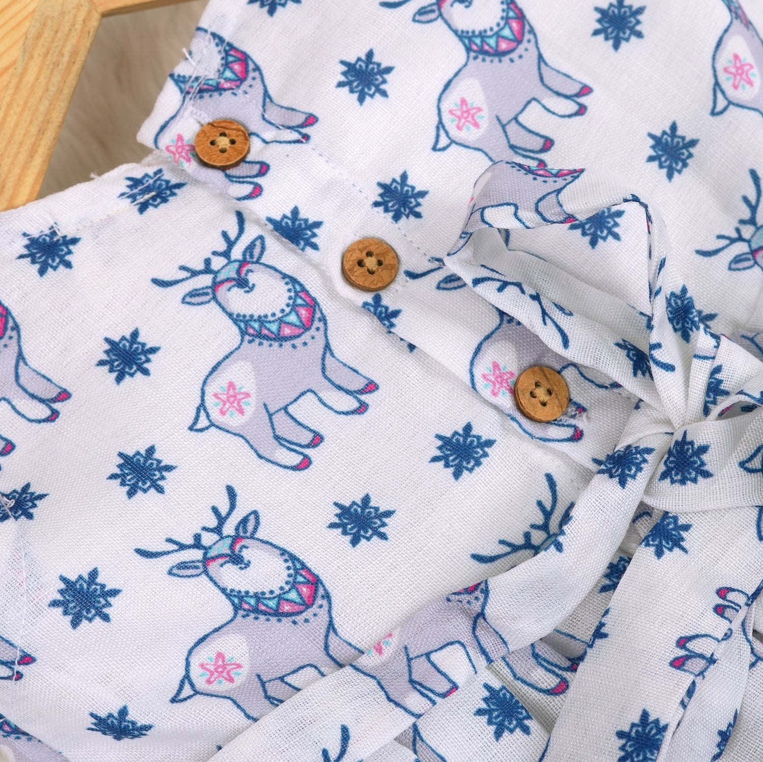 Baby girl wearing a white sleeveless frock with blue reindeer prints, made from slub cotton – part of the Boon Babies kidswear collection in Coimbatore.