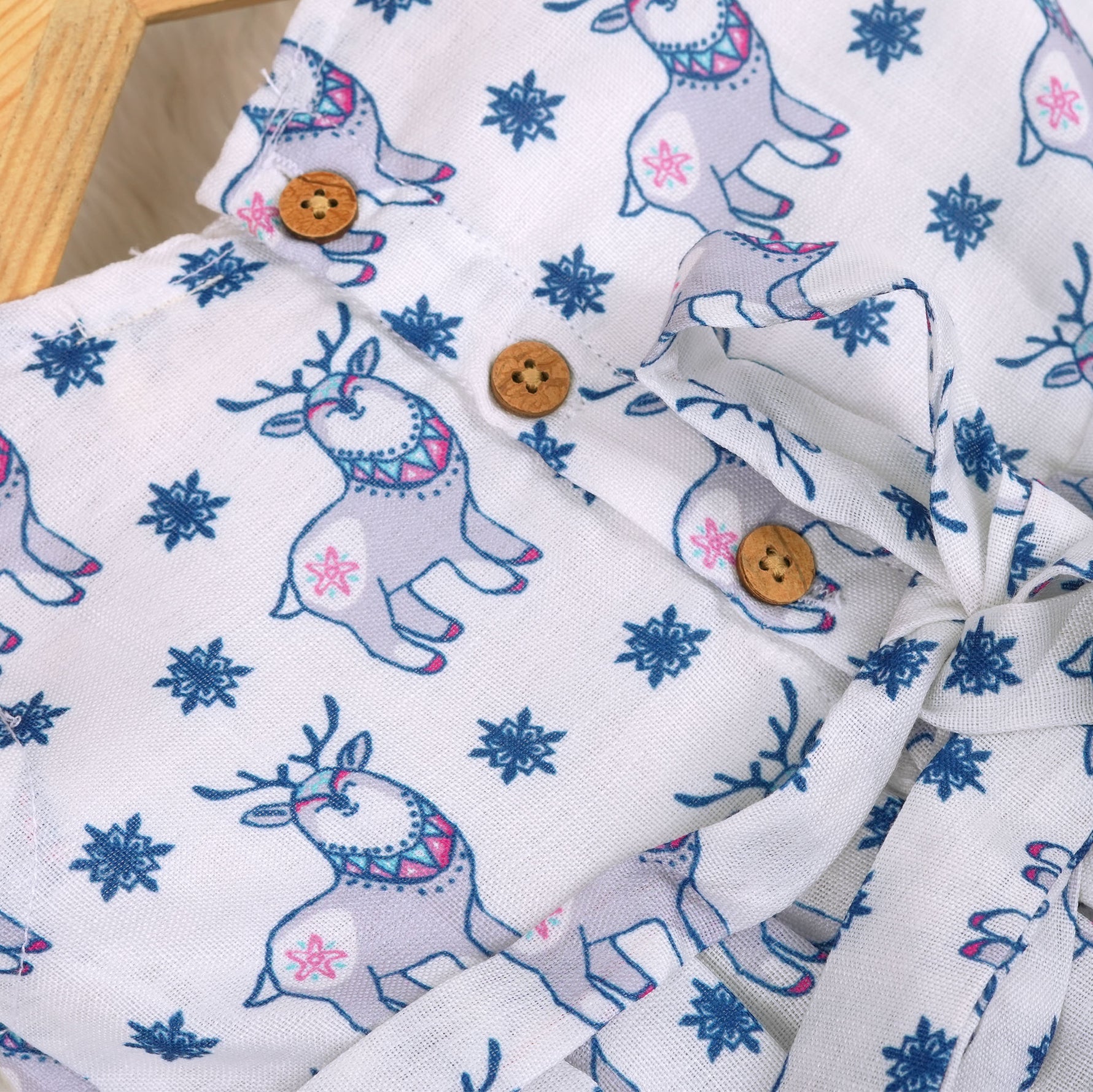 Baby girl wearing a white sleeveless frock with blue reindeer prints, made from slub cotton – part of the Boon Babies kidswear collection in Coimbatore.