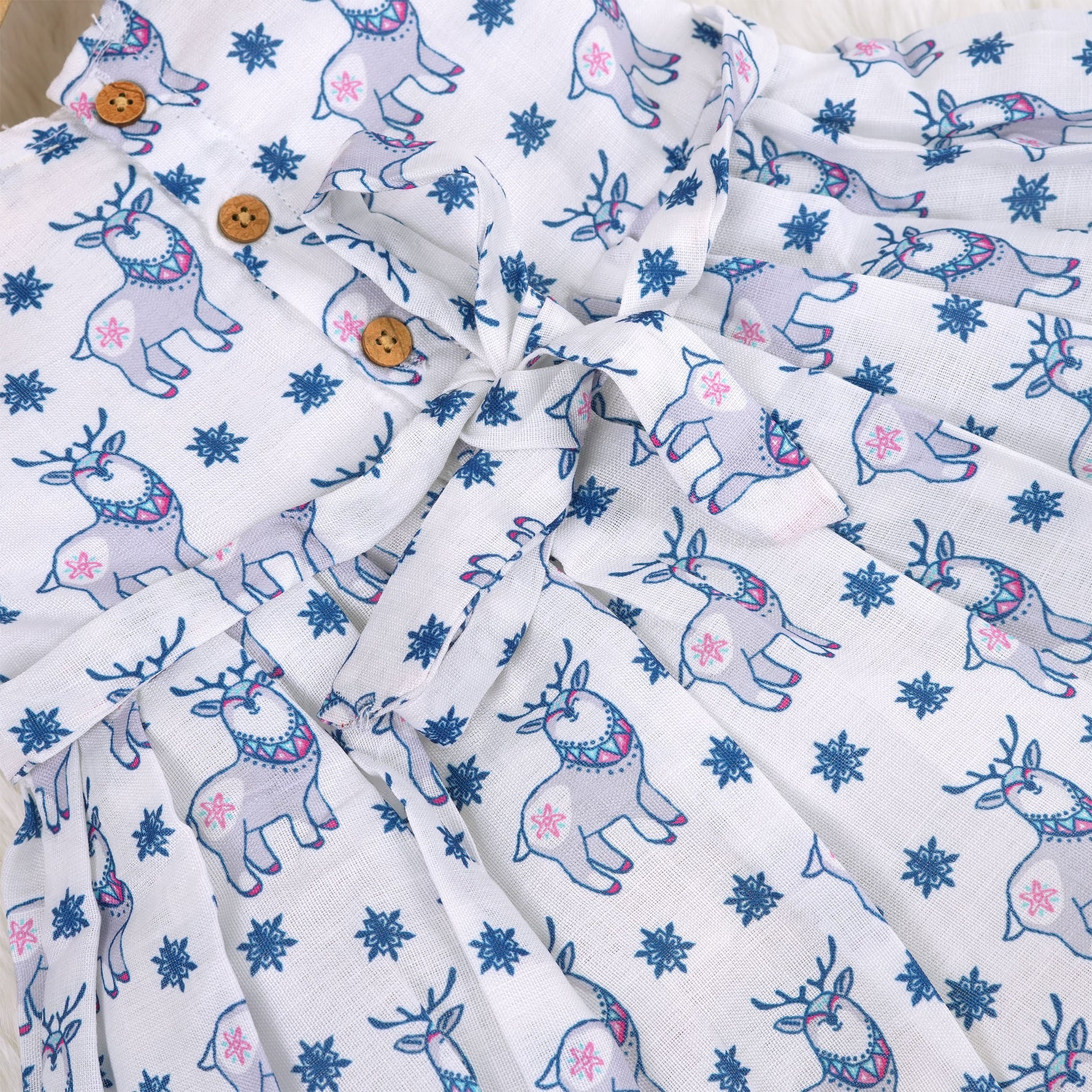 Baby girl wearing a white sleeveless frock with blue reindeer prints, made from slub cotton – part of the Boon Babies kidswear collection in Coimbatore.