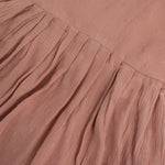 Brown crinkled cotton sleeveless frock for baby girls with pleated skirt design, displayed on a wooden hanger over a white faux fur background with floral accents.