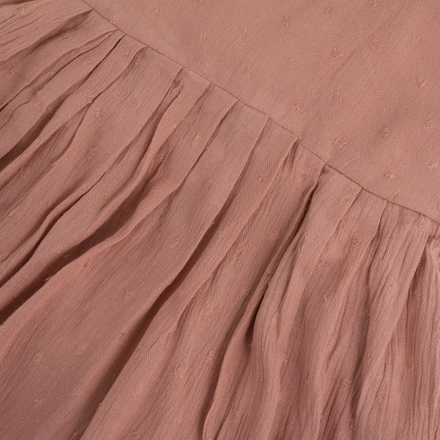 Brown crinkled cotton sleeveless frock for baby girls with pleated skirt design, displayed on a wooden hanger over a white faux fur background with floral accents.