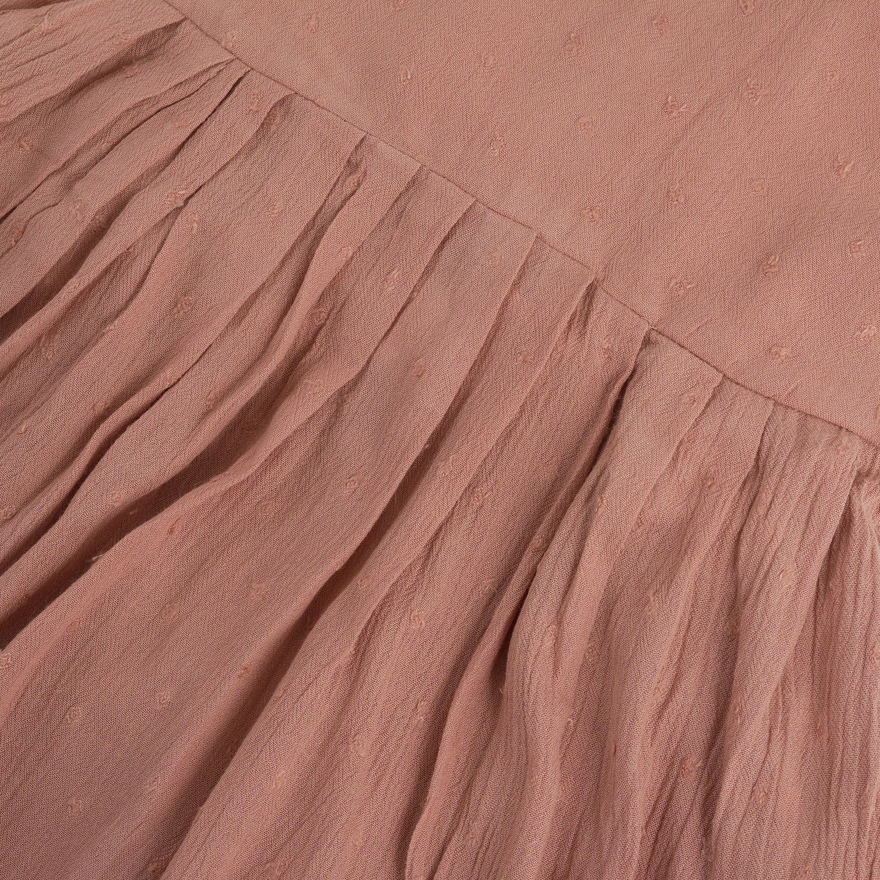 Brown crinkled cotton sleeveless frock for baby girls with pleated skirt design, displayed on a wooden hanger over a white faux fur background with floral accents.