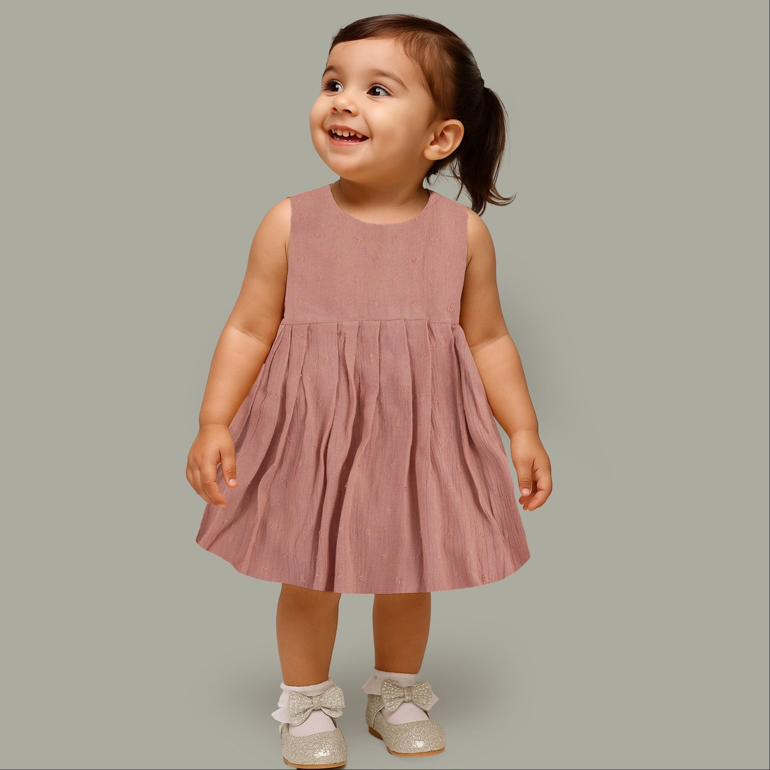 Brown crinkled cotton sleeveless frock for baby girls with pleated skirt design, displayed on a wooden hanger over a white faux fur background with floral accents.