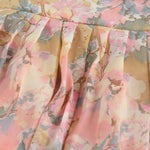 Floral printed sleeveless frock for baby girls in pastel shades of pink, beige, and grey, made from chiffon cotton and displayed on a wooden hanger over white fur with flower props.