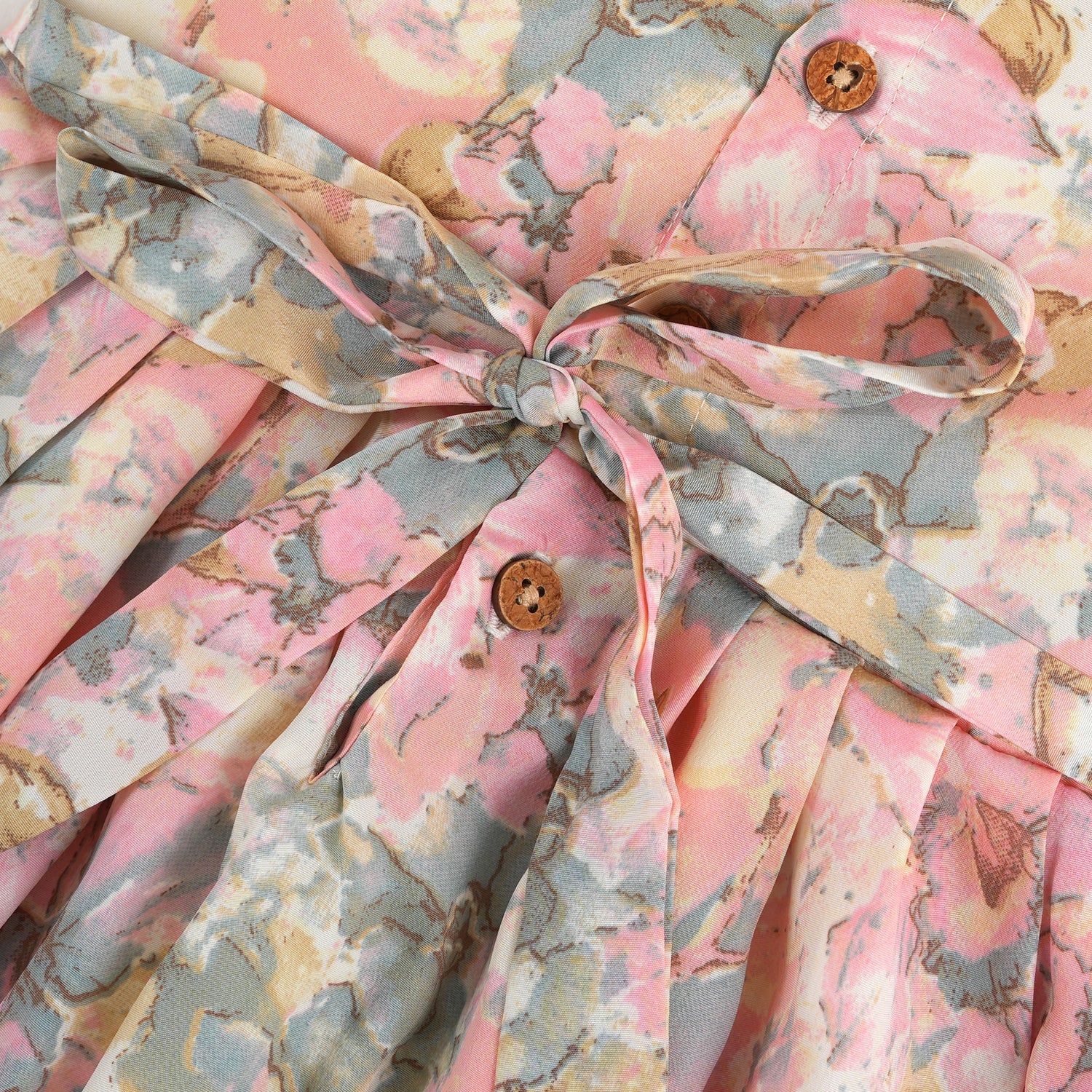 Floral printed sleeveless frock for baby girls in pastel shades of pink, beige, and grey, made from chiffon cotton and displayed on a wooden hanger over white fur with flower props.