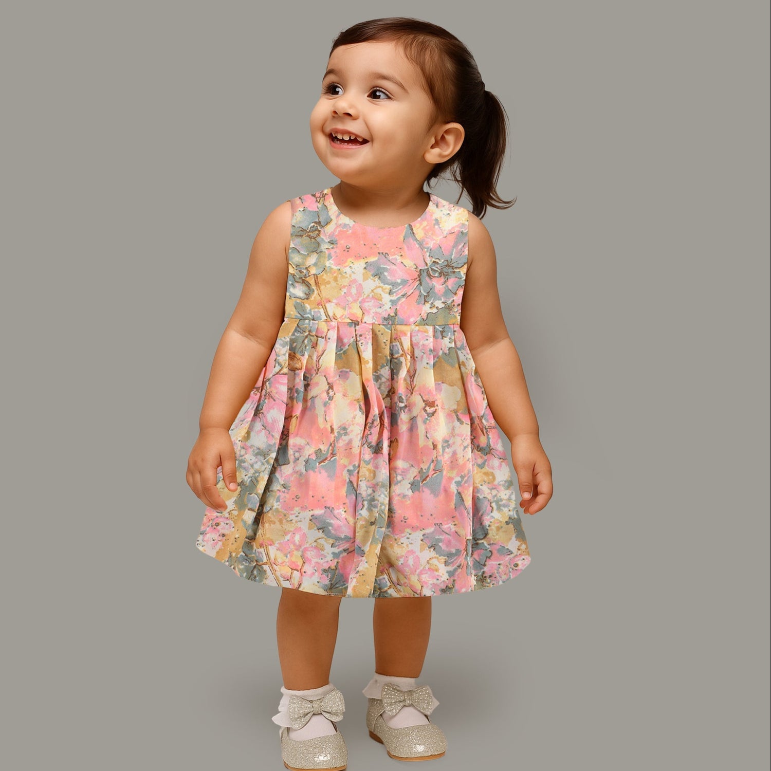 Floral printed sleeveless frock for baby girls in pastel shades of pink, beige, and grey, made from chiffon cotton and displayed on a wooden hanger over white fur with flower props.