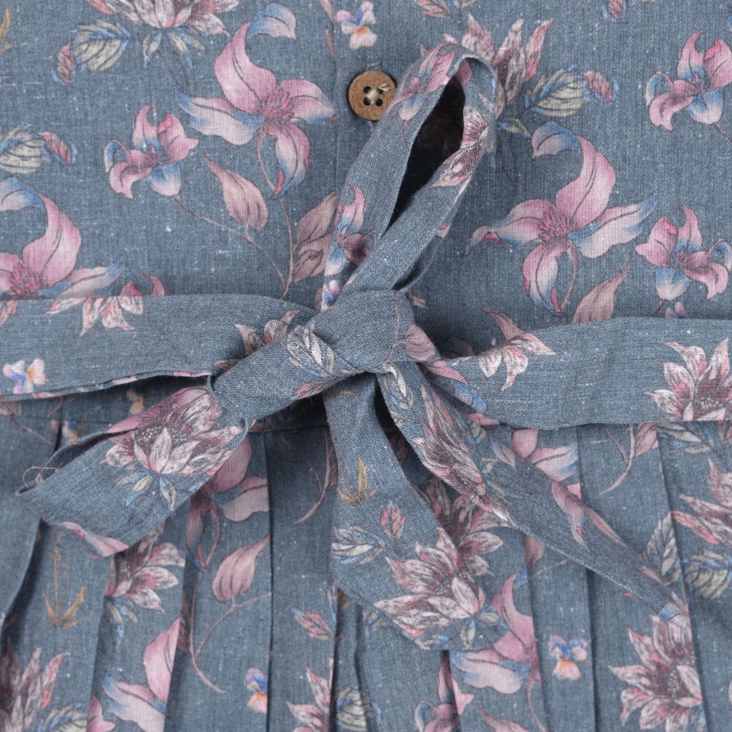 Sleeveless grey cotton frock with pink floral prints, neatly pleated and displayed on a wooden hanger under fresh orchids – from Boon Babies girlswear collection.
Sleeveless grey cotton frock with pink floral prints, neatly pleated and displayed on a wooden hanger under fresh orchids – from Boon Babies girlswear collection.
