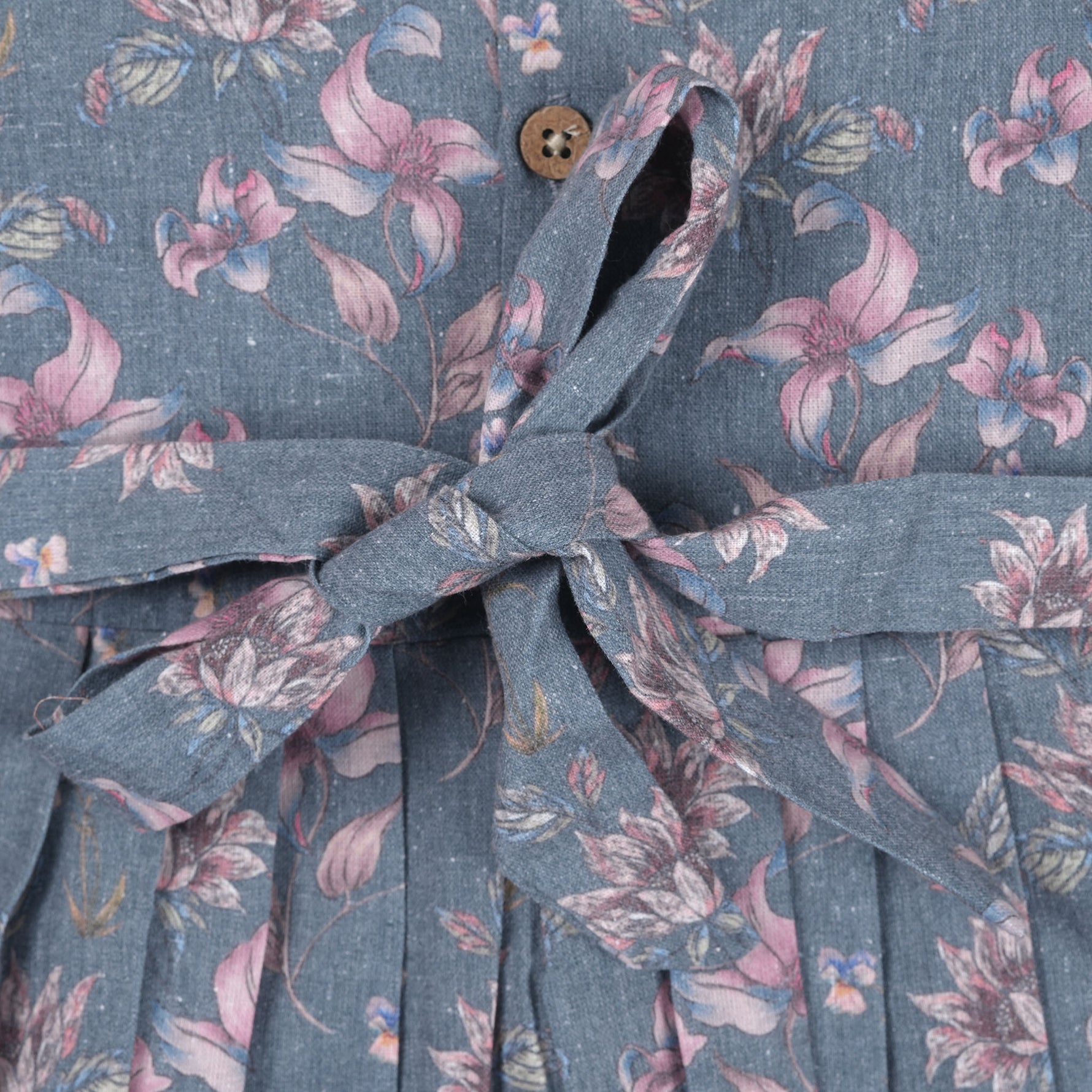 Sleeveless grey cotton frock with pink floral prints, neatly pleated and displayed on a wooden hanger under fresh orchids – from Boon Babies girlswear collection.
Sleeveless grey cotton frock with pink floral prints, neatly pleated and displayed on a wooden hanger under fresh orchids – from Boon Babies girlswear collection.
