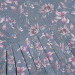 Sleeveless grey cotton frock with pink floral prints, neatly pleated and displayed on a wooden hanger under fresh orchids – from Boon Babies girlswear collection.
