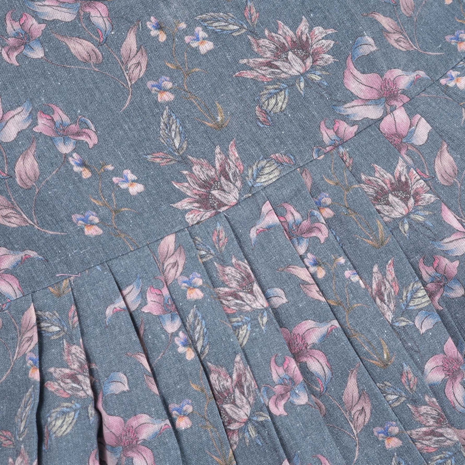 Sleeveless grey cotton frock with pink floral prints, neatly pleated and displayed on a wooden hanger under fresh orchids – from Boon Babies girlswear collection.

