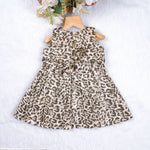 Leopard print sleeveless cotton frock for girls aged 12M–5Y, with a flared pleated skirt – displayed on a wooden hanger with white roses in the background.