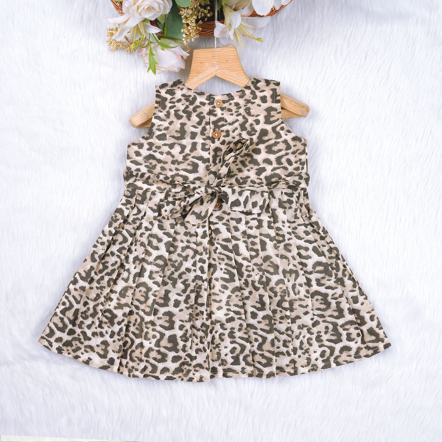 Leopard print sleeveless cotton frock for girls aged 12M–5Y, with a flared pleated skirt – displayed on a wooden hanger with white roses in the background.