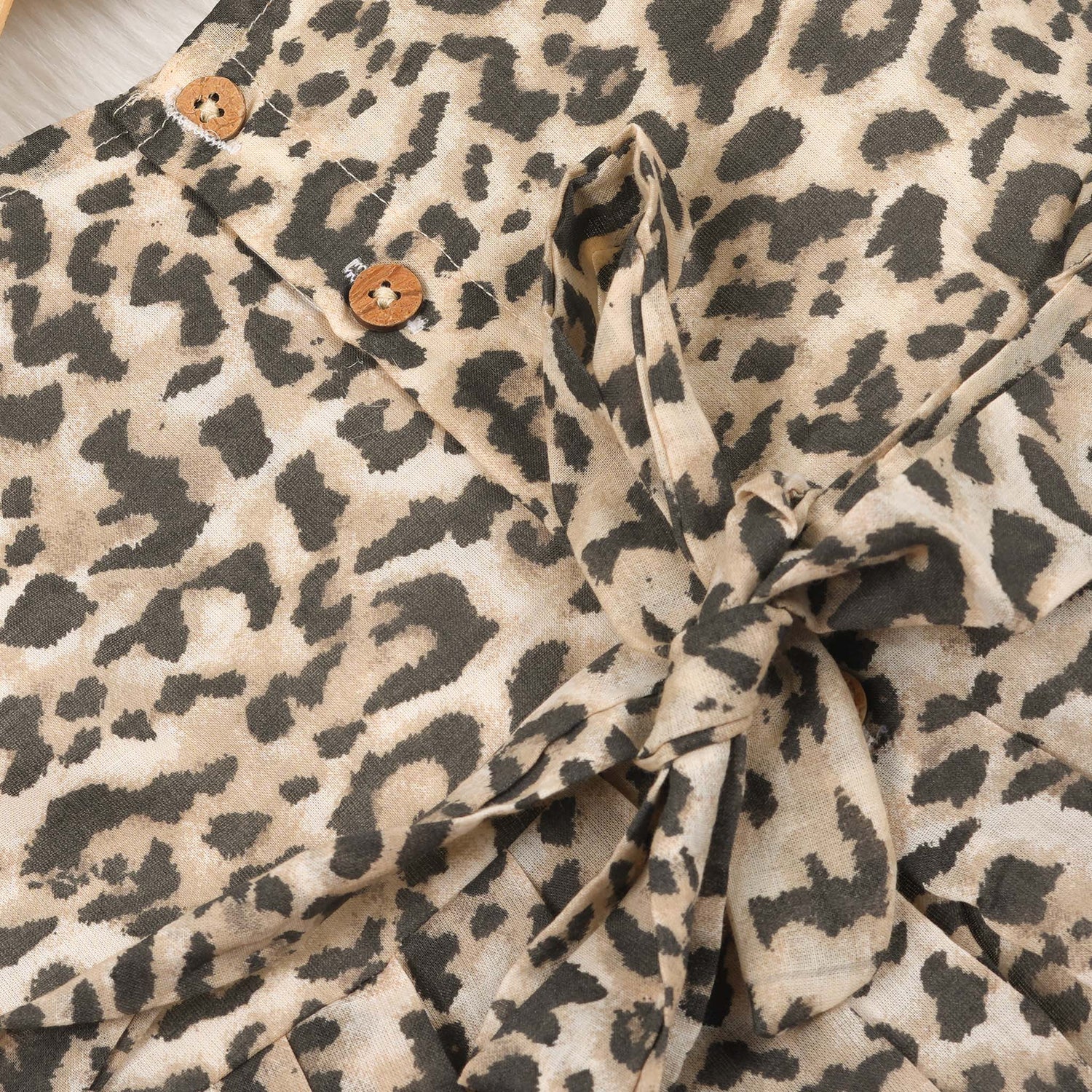 Leopard print sleeveless cotton frock for girls aged 12M–5Y, with a flared pleated skirt – displayed on a wooden hanger with white roses in the background.