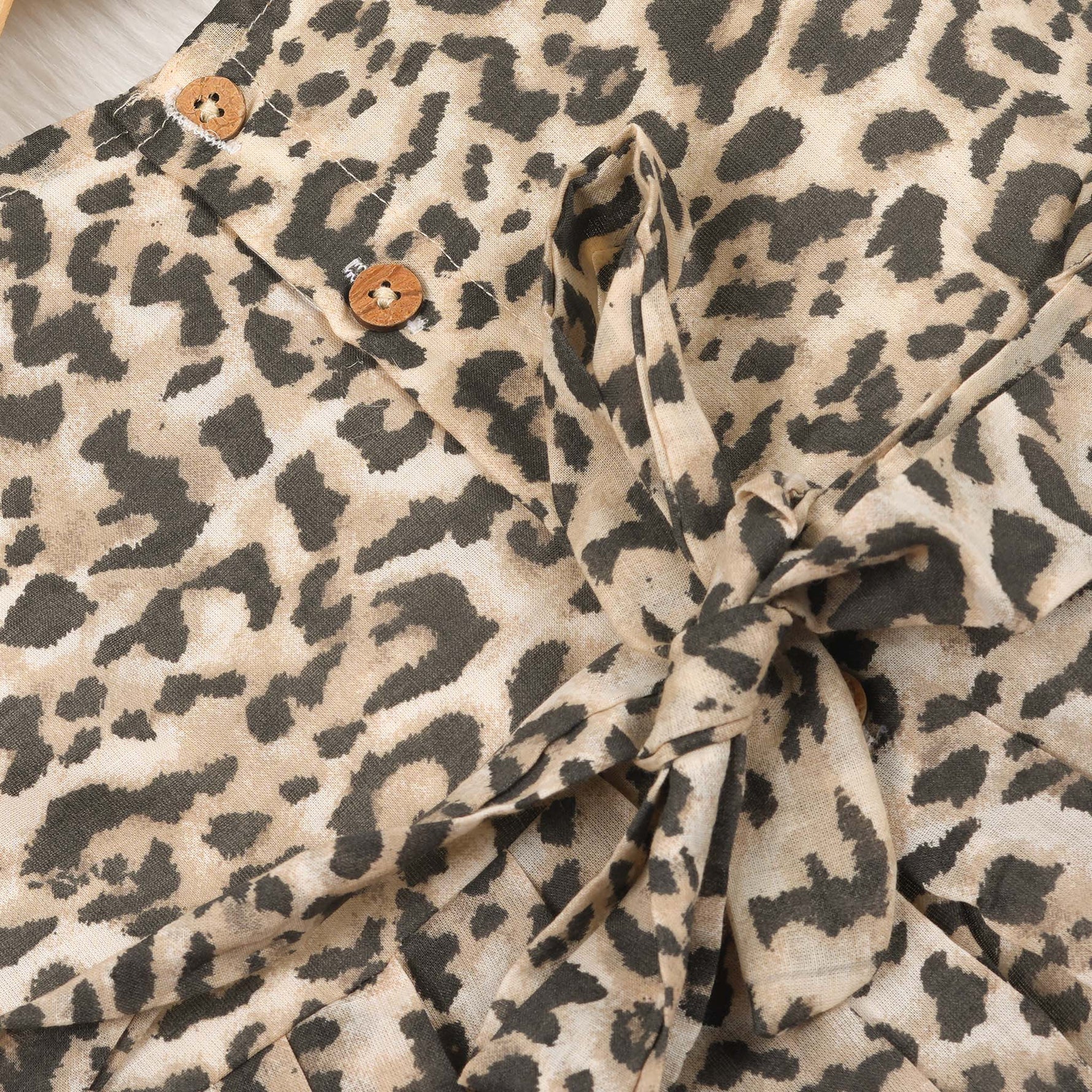 Leopard print sleeveless cotton frock for girls aged 12M–5Y, with a flared pleated skirt – displayed on a wooden hanger with white roses in the background.