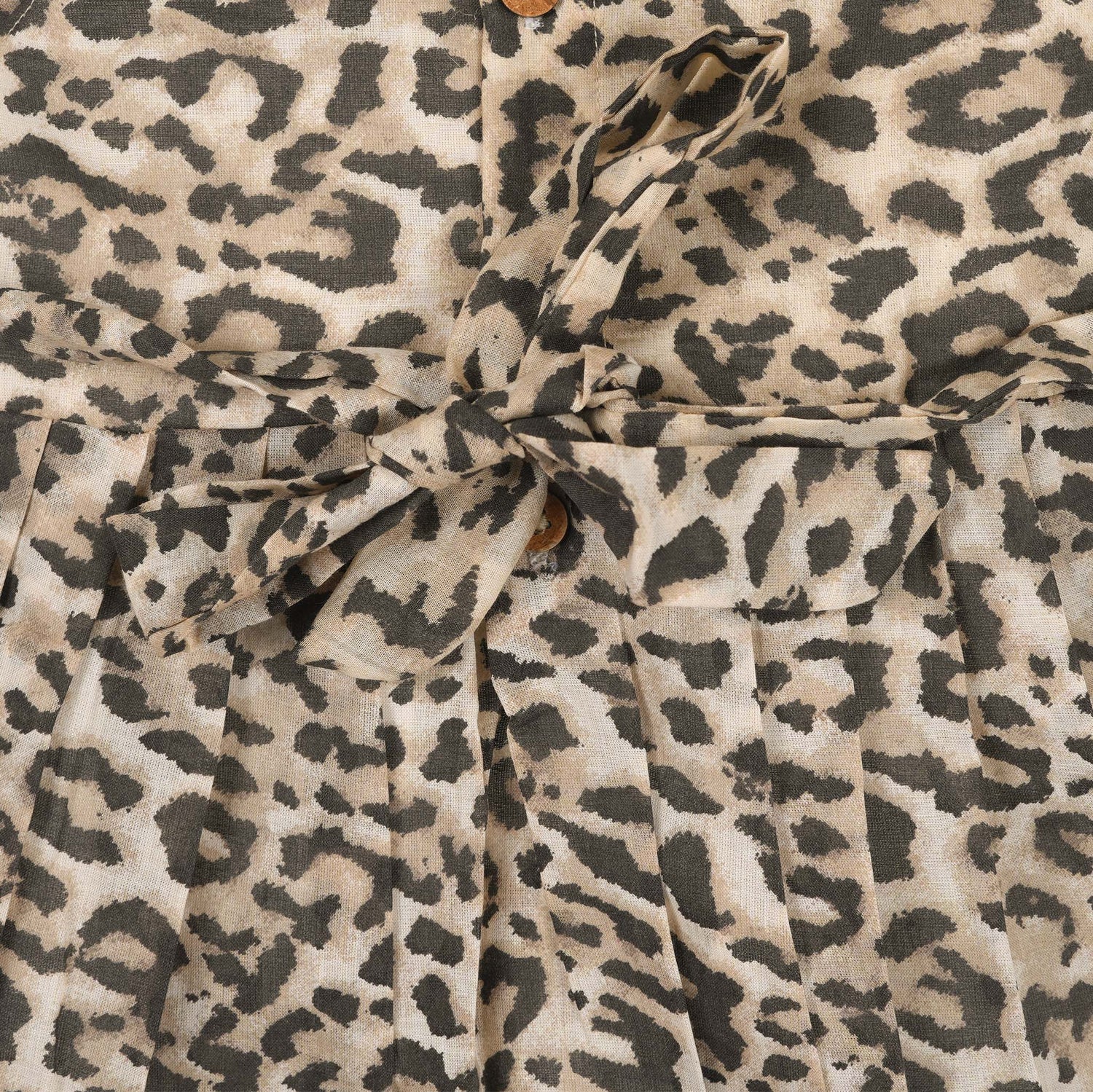 Leopard print sleeveless cotton frock for girls aged 12M–5Y, with a flared pleated skirt – displayed on a wooden hanger with white roses in the background.