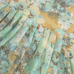 Mint green floral sleeveless chiffon cotton frock for baby girls, pleated and lightweight, displayed on a wooden hanger over a white fur backdrop with pink and white flowers.