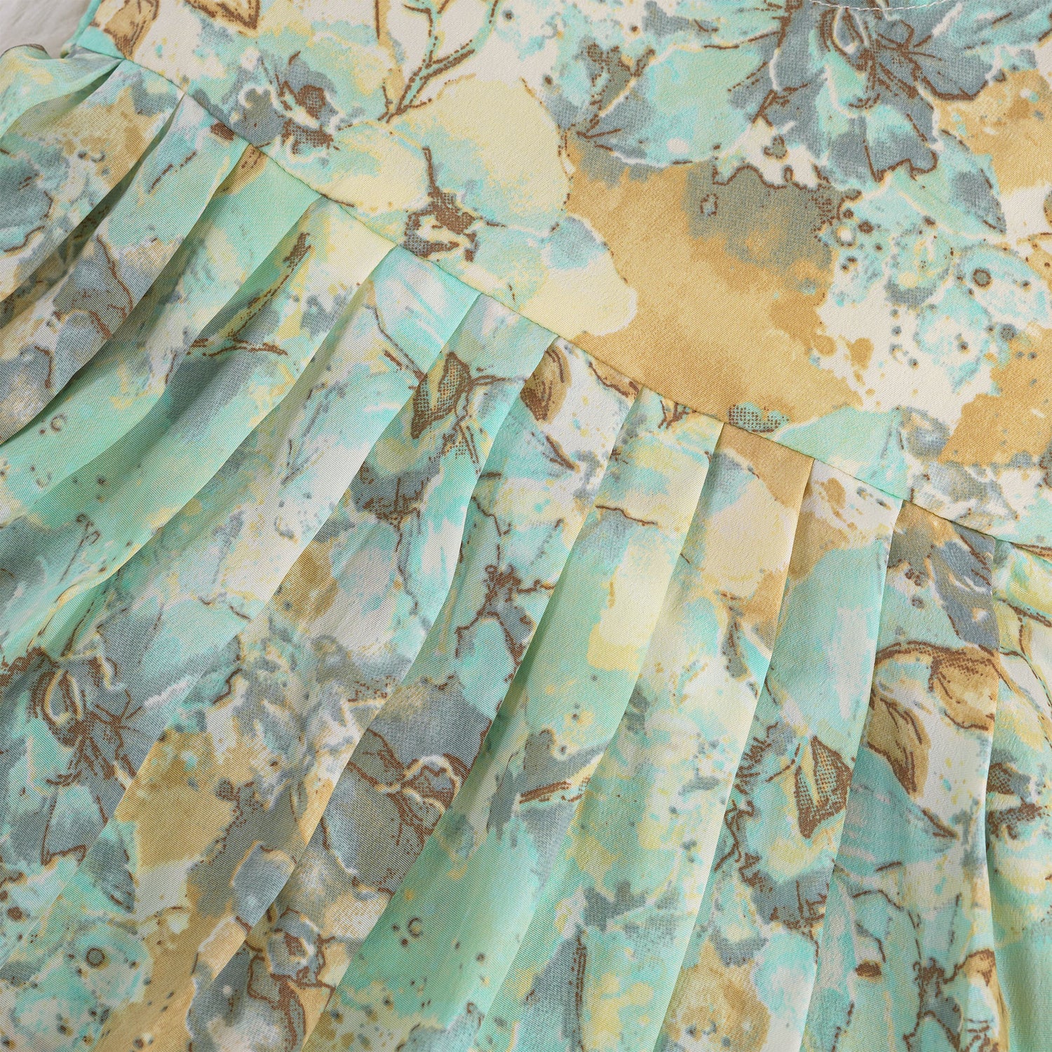 Mint green floral sleeveless chiffon cotton frock for baby girls, pleated and lightweight, displayed on a wooden hanger over a white fur backdrop with pink and white flowers.