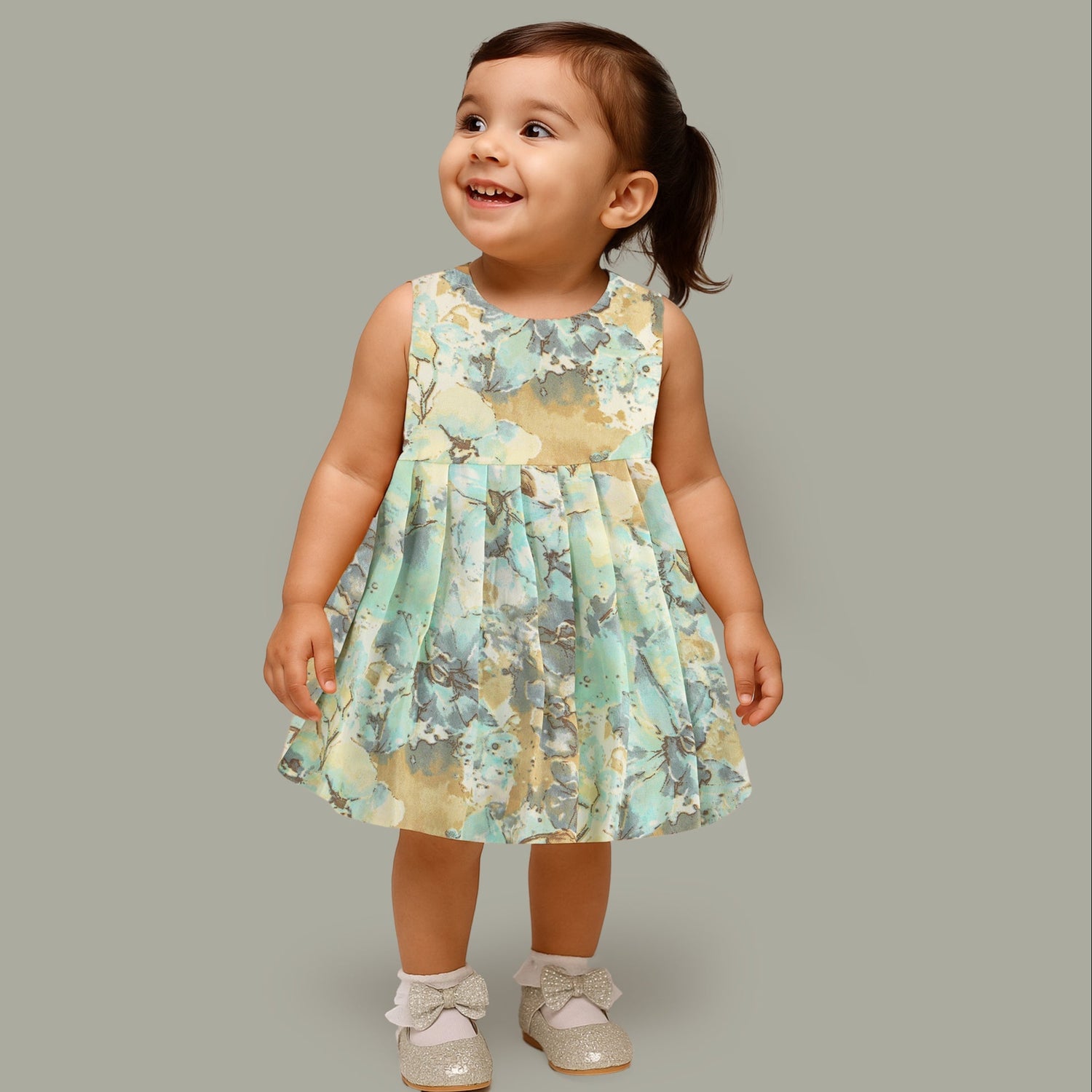 Mint green floral sleeveless chiffon cotton frock for baby girls, pleated and lightweight, displayed on a wooden hanger over a white fur backdrop with pink and white flowers.