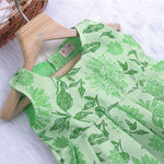 Mint green floral printed sleeveless slub cotton frock for baby girls with pleated flare, displayed flat on white fur background with floral basket hanger.