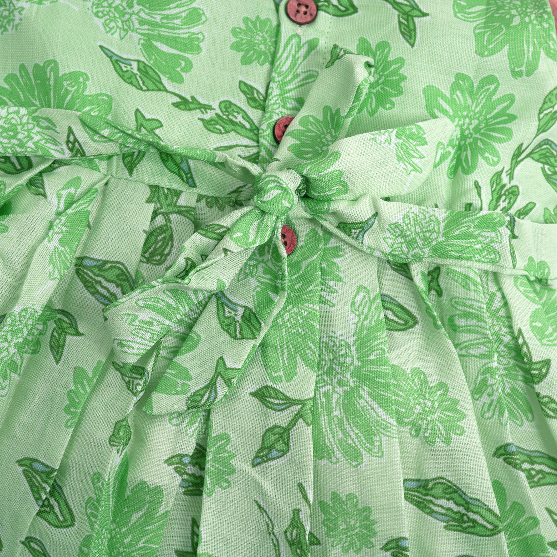 Mint green floral printed sleeveless slub cotton frock for baby girls with pleated flare, displayed flat on white fur background with floral basket hanger.