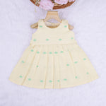 Pastel yellow sleeveless cotton frock with mint green embroidery and pleated skirt for baby girls, displayed on a white fur background with floral basket hanger.