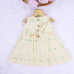 Pastel yellow sleeveless cotton frock with mint green embroidery and pleated skirt for baby girls, displayed on a white fur background with floral basket hanger.