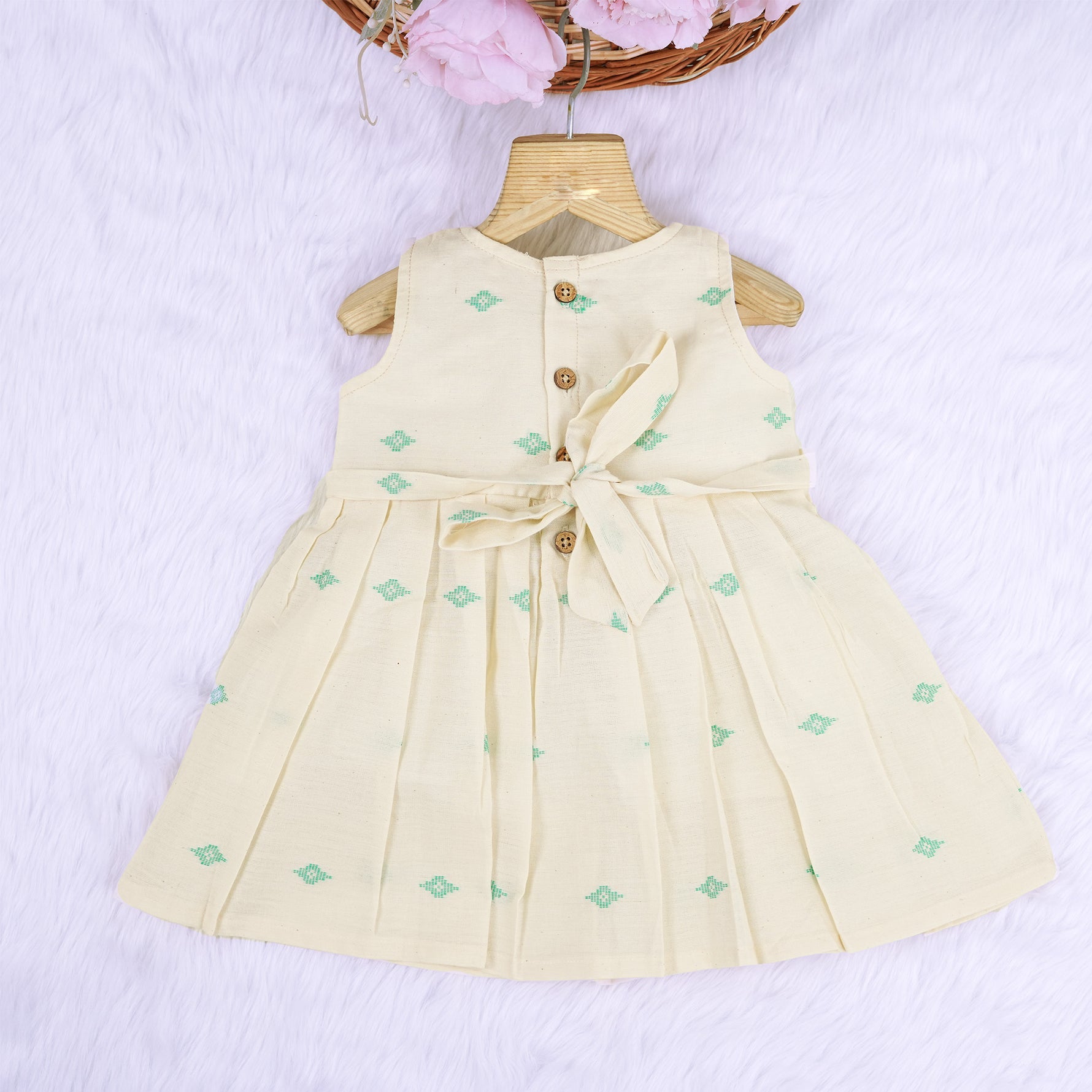 Pastel yellow sleeveless cotton frock with mint green embroidery and pleated skirt for baby girls, displayed on a white fur background with floral basket hanger.