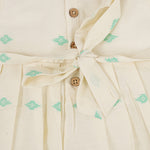 Pastel yellow sleeveless cotton frock with mint green embroidery and pleated skirt for baby girls, displayed on a white fur background with floral basket hanger.