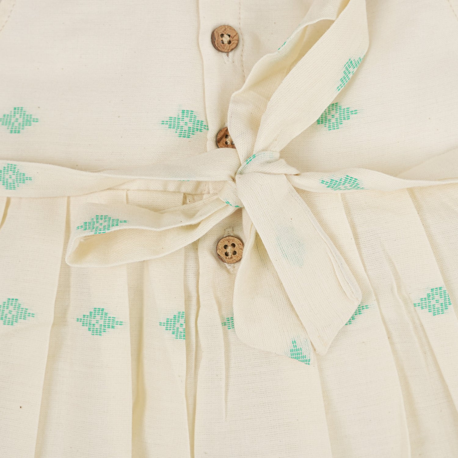 Pastel yellow sleeveless cotton frock with mint green embroidery and pleated skirt for baby girls, displayed on a white fur background with floral basket hanger.