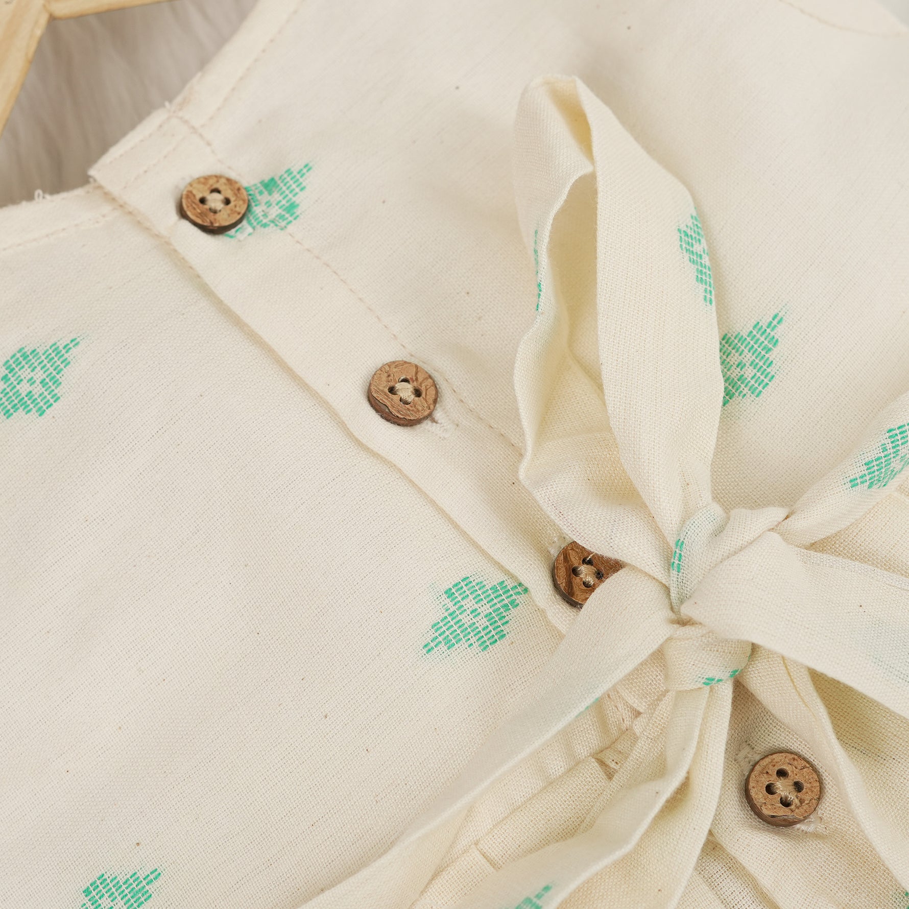 Pastel yellow sleeveless cotton frock with mint green embroidery and pleated skirt for baby girls, displayed on a white fur background with floral basket hanger.