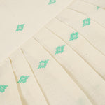 Pastel yellow sleeveless cotton frock with mint green embroidery and pleated skirt for baby girls, displayed on a white fur background with floral basket hanger.