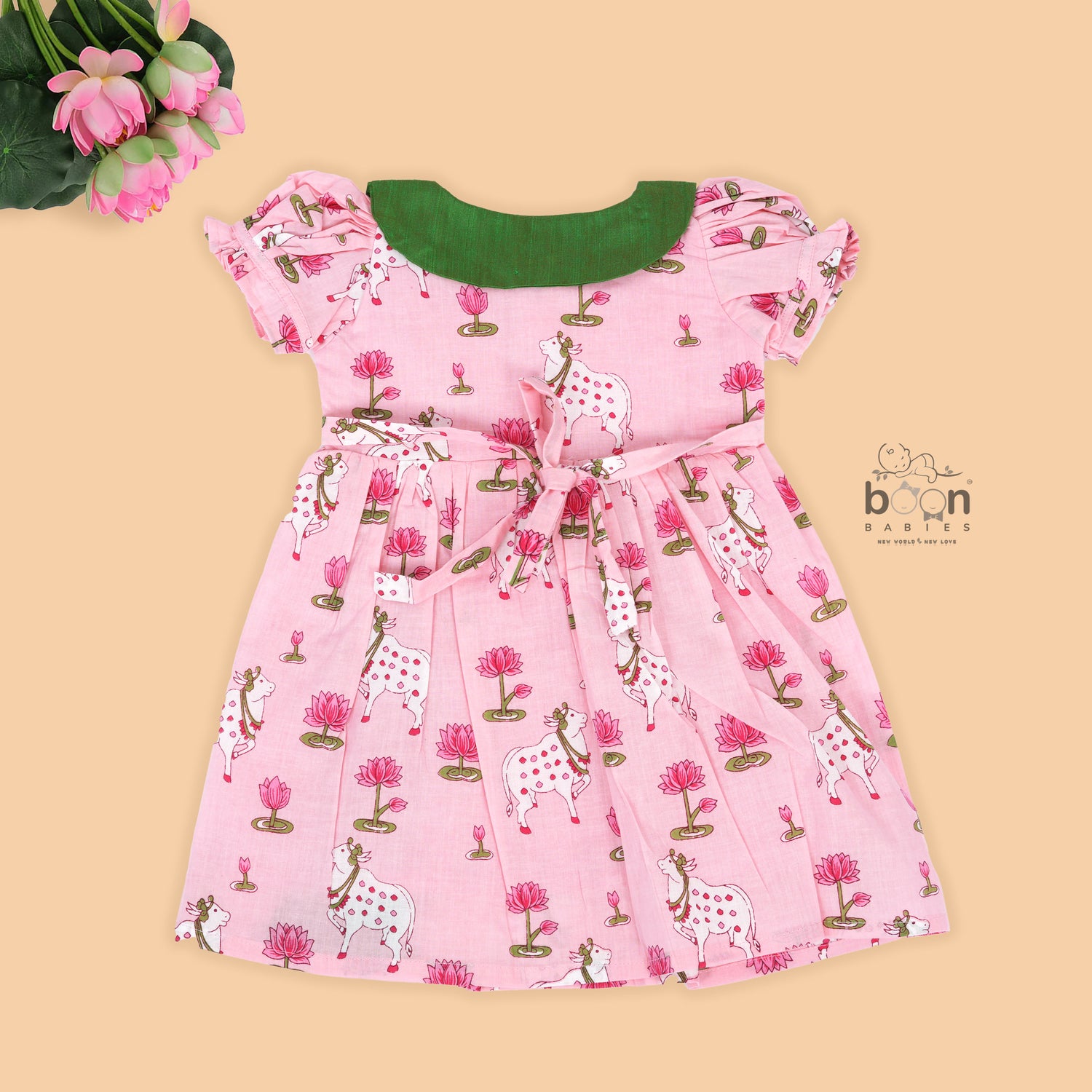 Pink cotton puff frock with green bow, contrast collar & lotus cow print. Cute, festive & comfy for baby girls aged 6M–4Y.