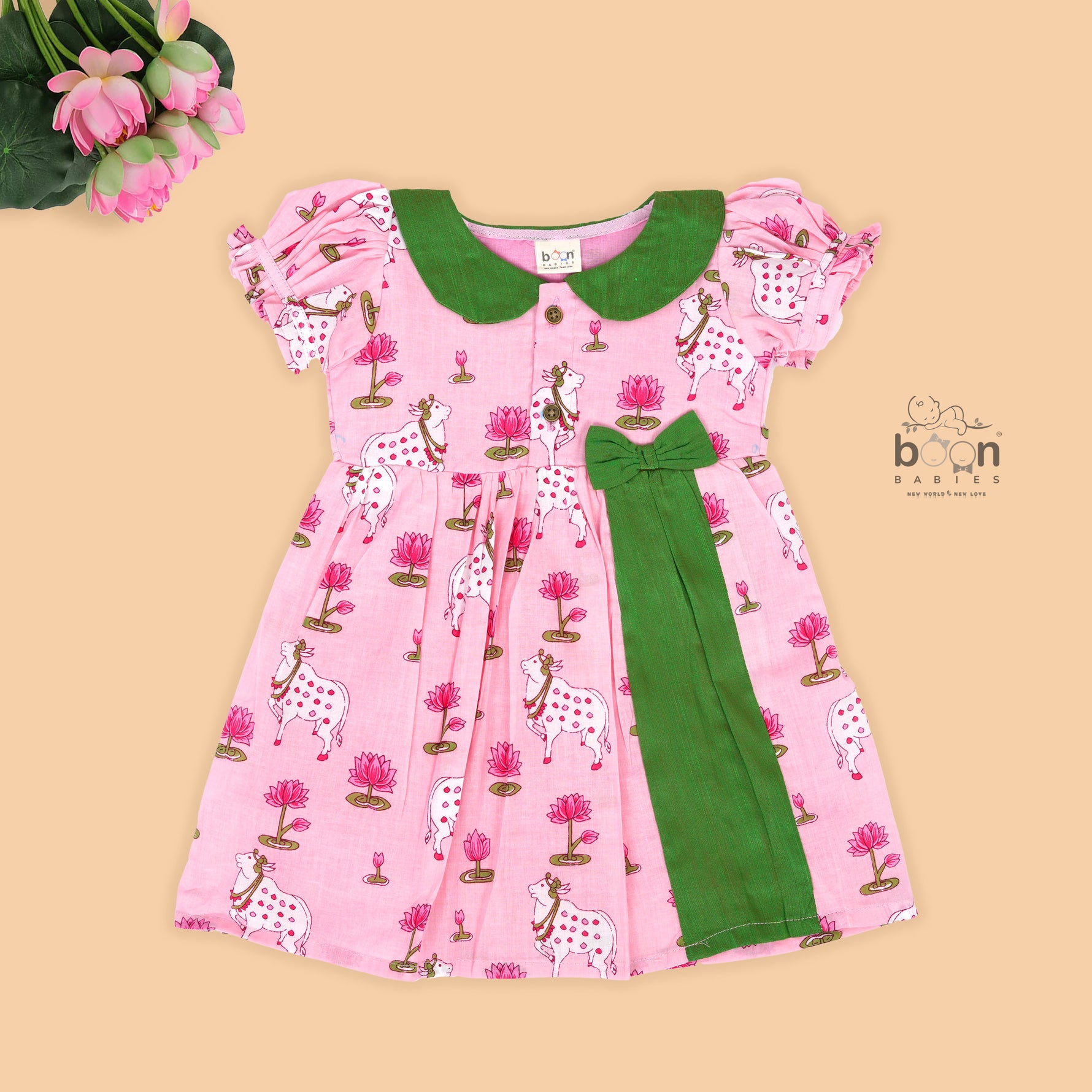 Pink cotton puff frock with green bow, contrast collar & lotus cow print. Cute, festive & comfy for baby girls aged 6M–4Y.