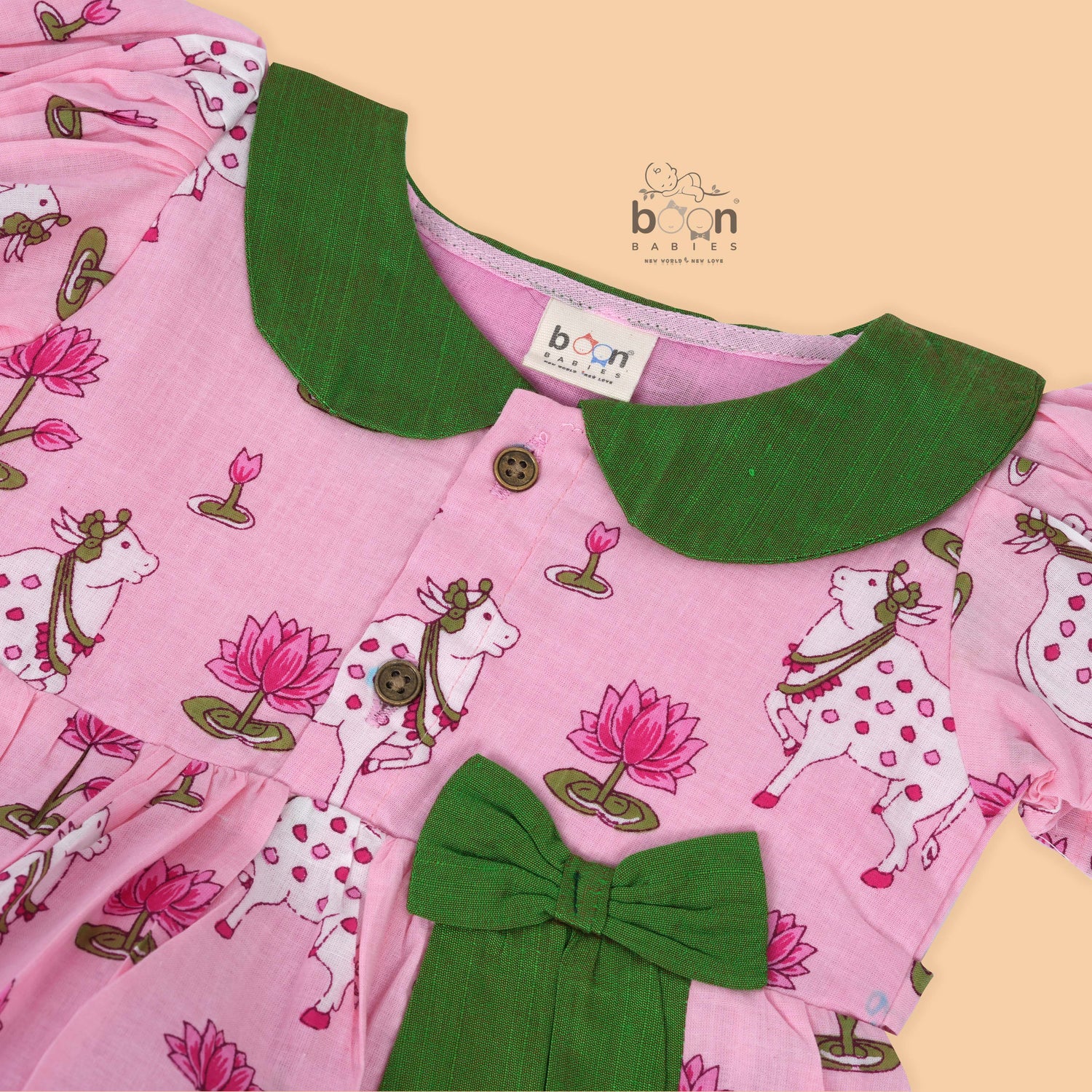 Pink cotton puff frock with green bow, contrast collar & lotus cow print. Cute, festive & comfy for baby girls aged 6M–4Y.
