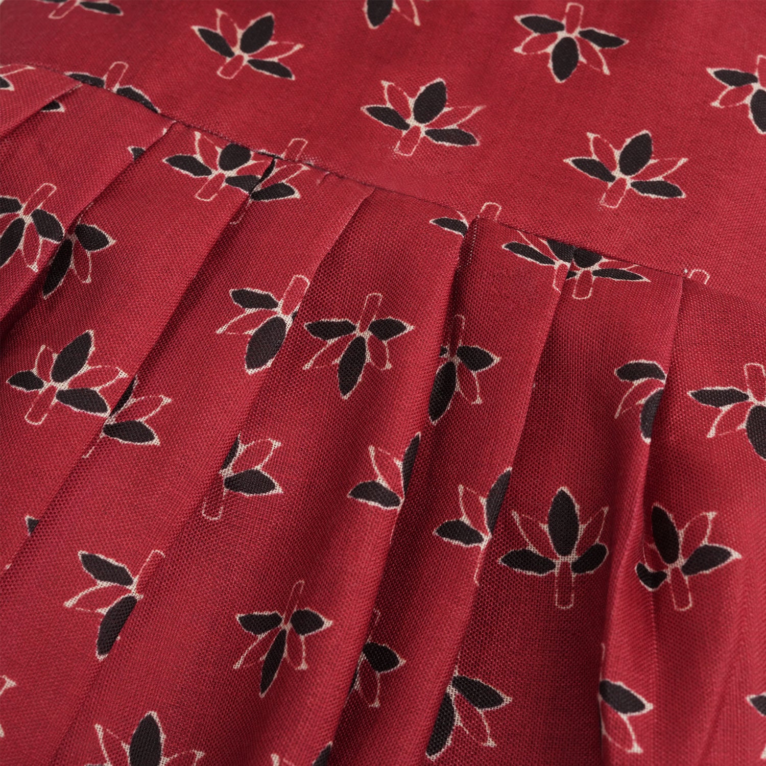 Rust orange sleeveless slub cotton frock for baby girls with black floral prints and pleated skirt, displayed on a white fur background with floral basket hanger.