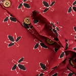 Rust orange sleeveless slub cotton frock for baby girls with black floral prints and pleated skirt, displayed on a white fur background with floral basket hanger.