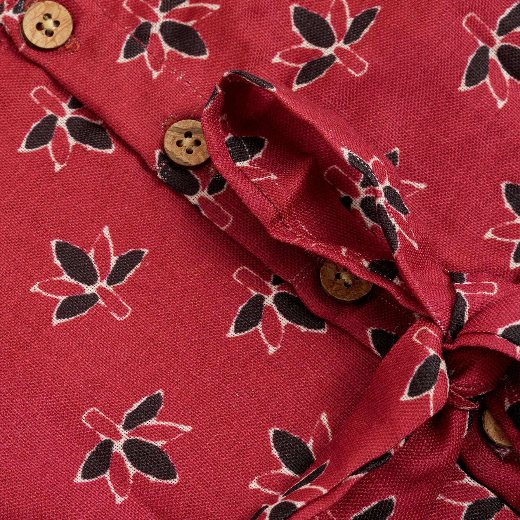 Rust orange sleeveless slub cotton frock for baby girls with black floral prints and pleated skirt, displayed on a white fur background with floral basket hanger.