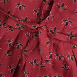 Rust orange sleeveless slub cotton frock for baby girls with black floral prints and pleated skirt, displayed on a white fur background with floral basket hanger.