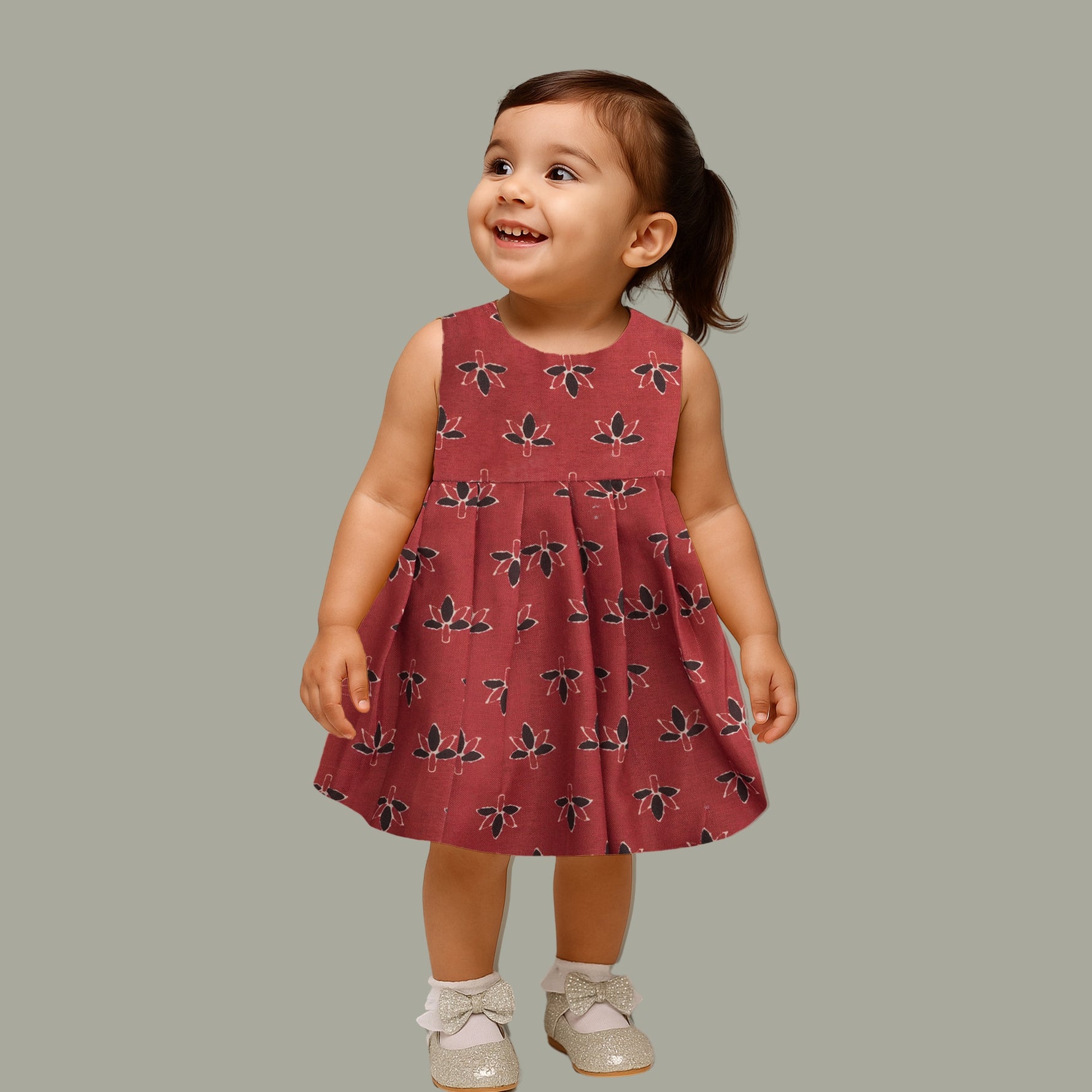 Rust orange sleeveless slub cotton frock for baby girls with black floral prints and pleated skirt, displayed on a white fur background with floral basket hanger.