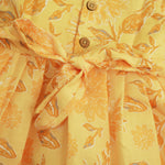 Sunshine yellow sleeveless slub cotton frock for baby girls with all-over orange floral print and pleated skirt, displayed flat on a white fur background with floral basket hanger.